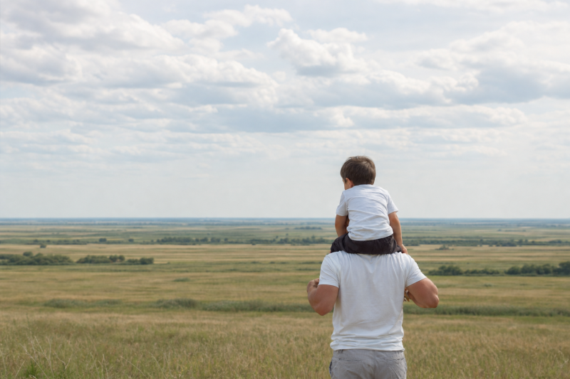 Vader met zijn zoontje op de schouders kijkt uit over een weids landschap